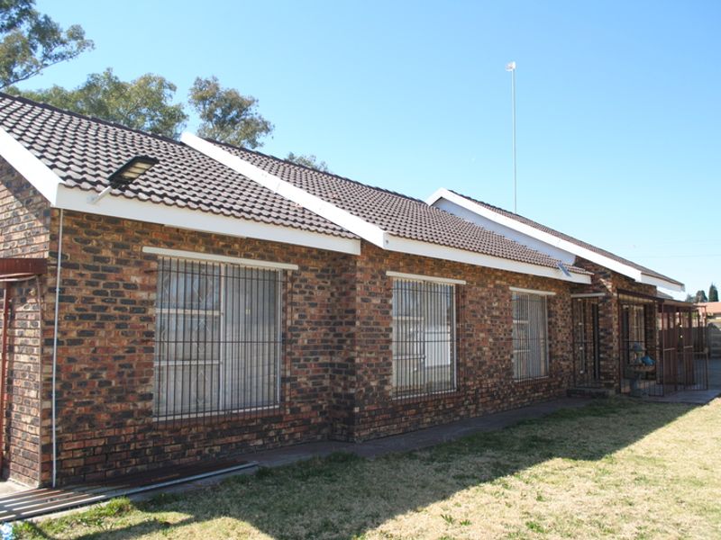 Rear view of a face brick house featuring a tiled roof, security bars on windows, and a security gate.