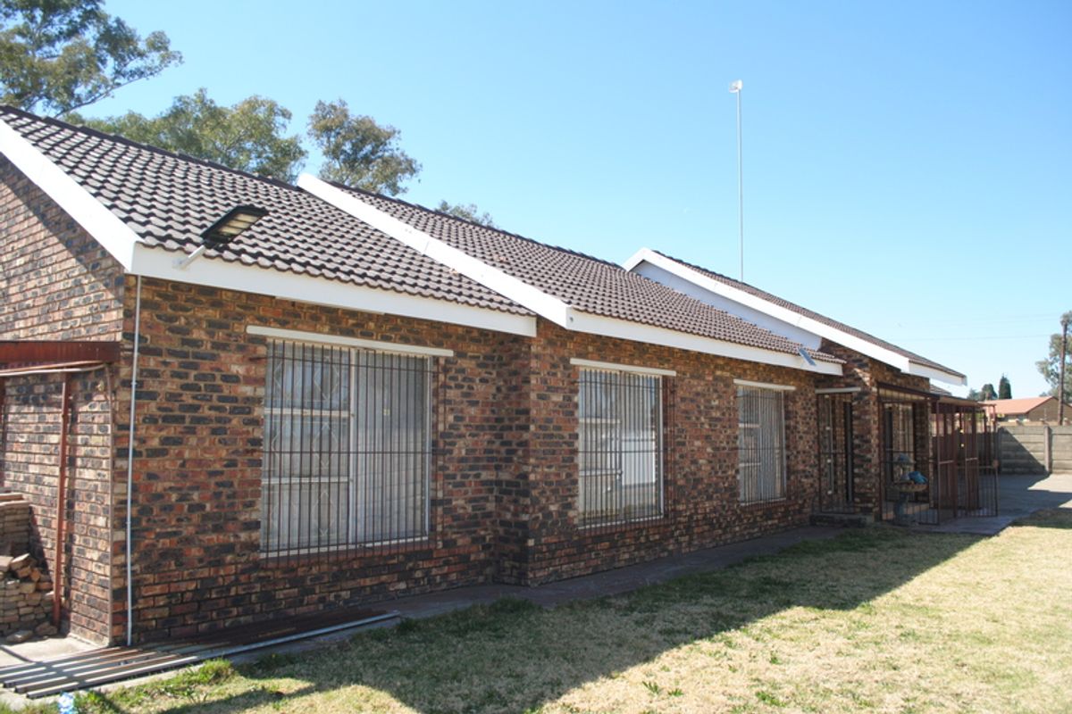 Rear view of a face brick house featuring a tiled roof, security bars on windows, and a security gate.