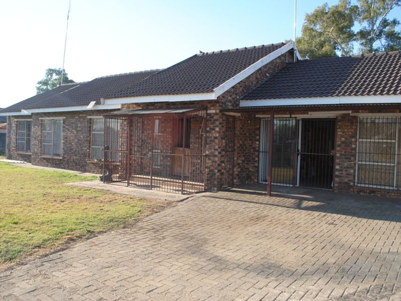 Front exterior view of a single-story face brick house featuring a tiled roof, paved driveway, and security-fitted entrances.