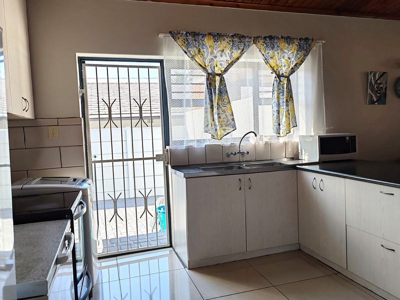 A functional kitchen featuring built-in cabinetry, tiled flooring, a stainless steel double sink, and direct access to the exterior via a security gate.