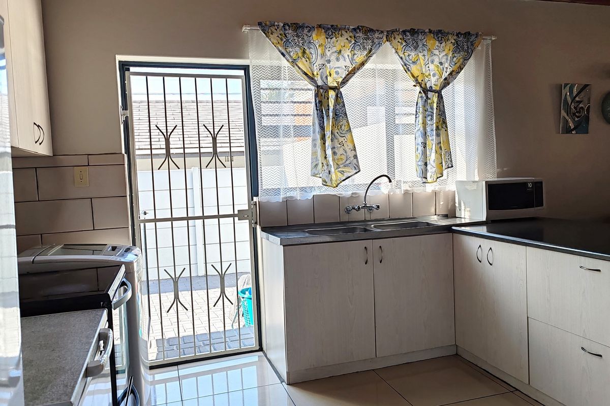 A functional kitchen featuring built-in cabinetry, tiled flooring, a stainless steel double sink, and direct access to the exterior via a security gate.