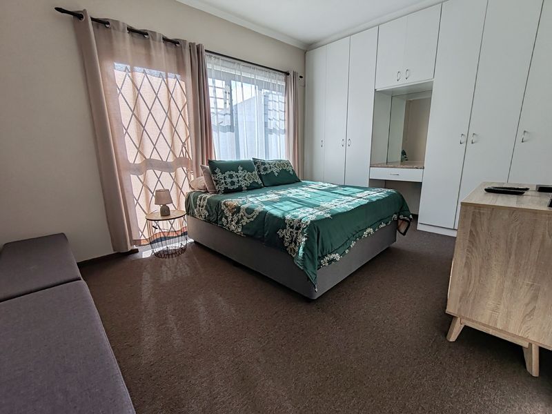 Spacious bedroom featuring extensive built-in cupboards with an integrated vanity area, carpeted flooring, and direct access to the exterior via a sliding door.