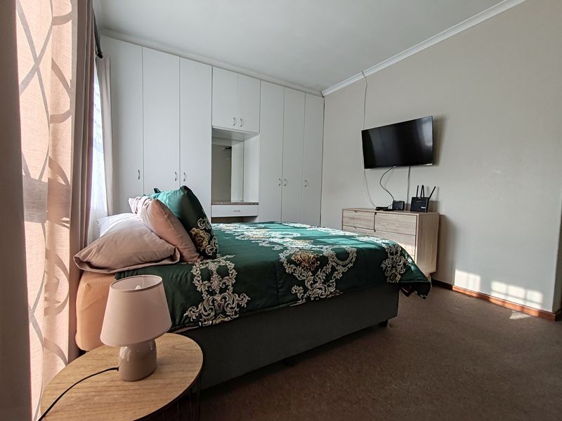 A well-lit bedroom featuring extensive built-in cupboards with an integrated vanity mirror and neutral wall finishes.