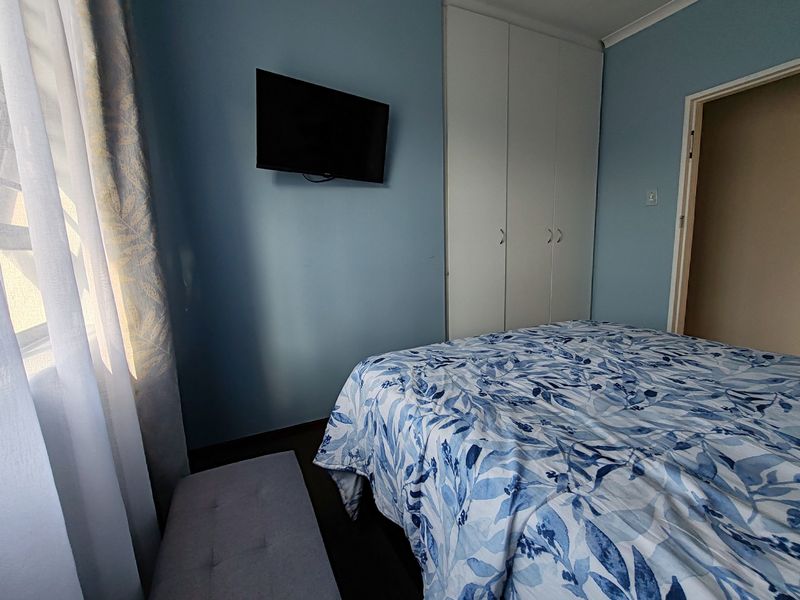 A bedroom featuring blue painted walls, built-in white wardrobes, and a wall-mounted television.