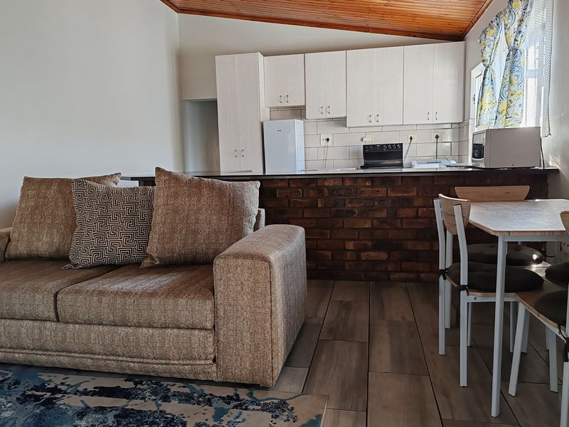 Open-plan living and kitchen area featuring a brick breakfast bar, exposed timber ceiling, and tiled flooring throughout.