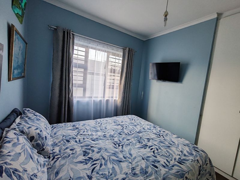 A cozy bedroom featuring blue walls, a built-in wardrobe, and a window fitted with security bars.
