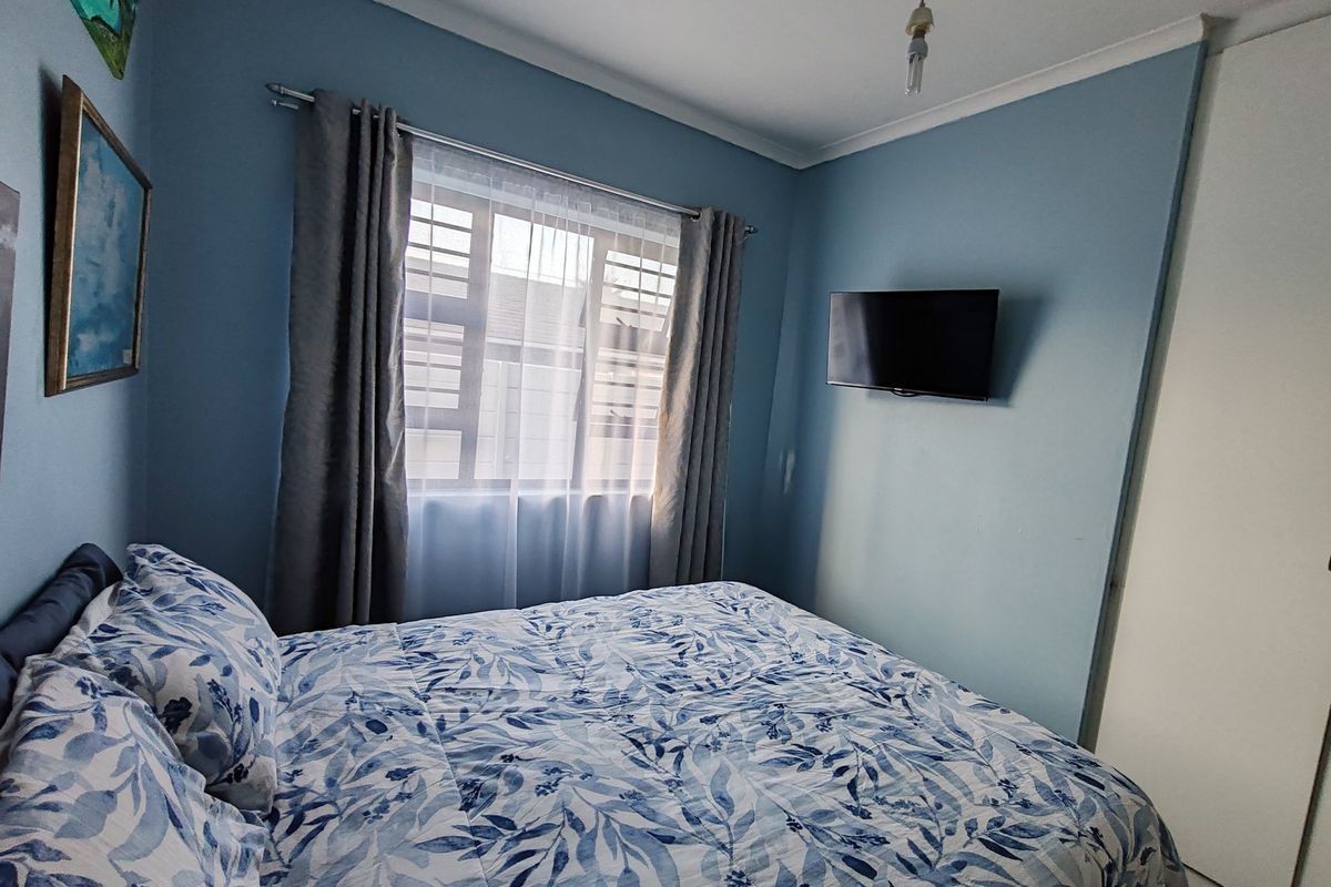 A cozy bedroom featuring blue walls, a built-in wardrobe, and a window fitted with security bars.