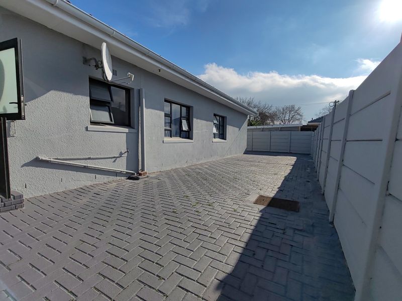 A paved rear exterior area featuring a clean concrete boundary wall, external plumbing access, and a satellite dish installation.