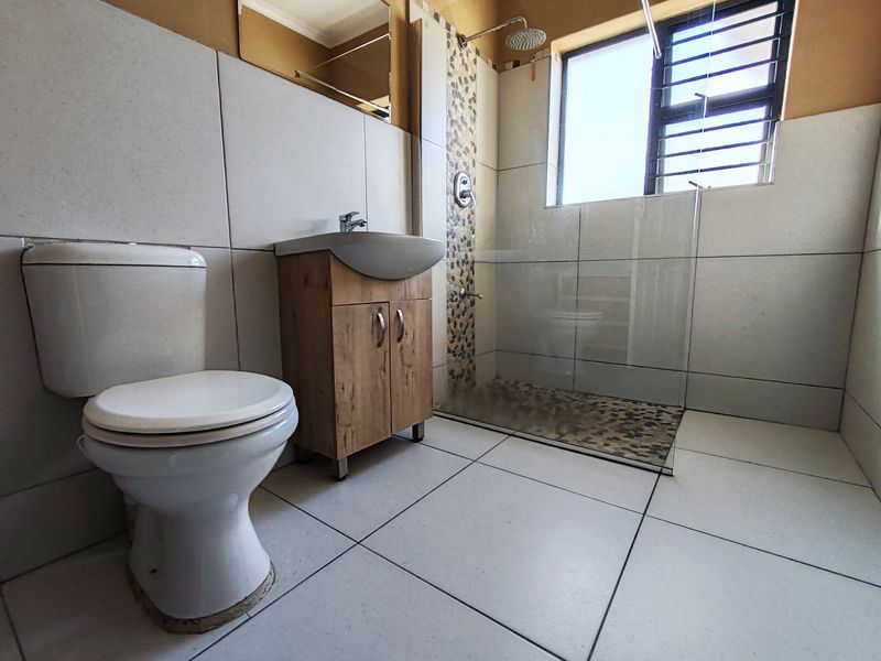 A functional bathroom featuring a walk-in shower with pebble-tiled floor, a modern vanity unit, and neutral wall tiling.