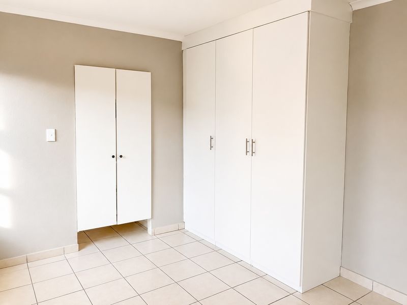 A clean, empty bedroom featuring neutral wall tones, tiled flooring, and ample built-in cupboard storage space.