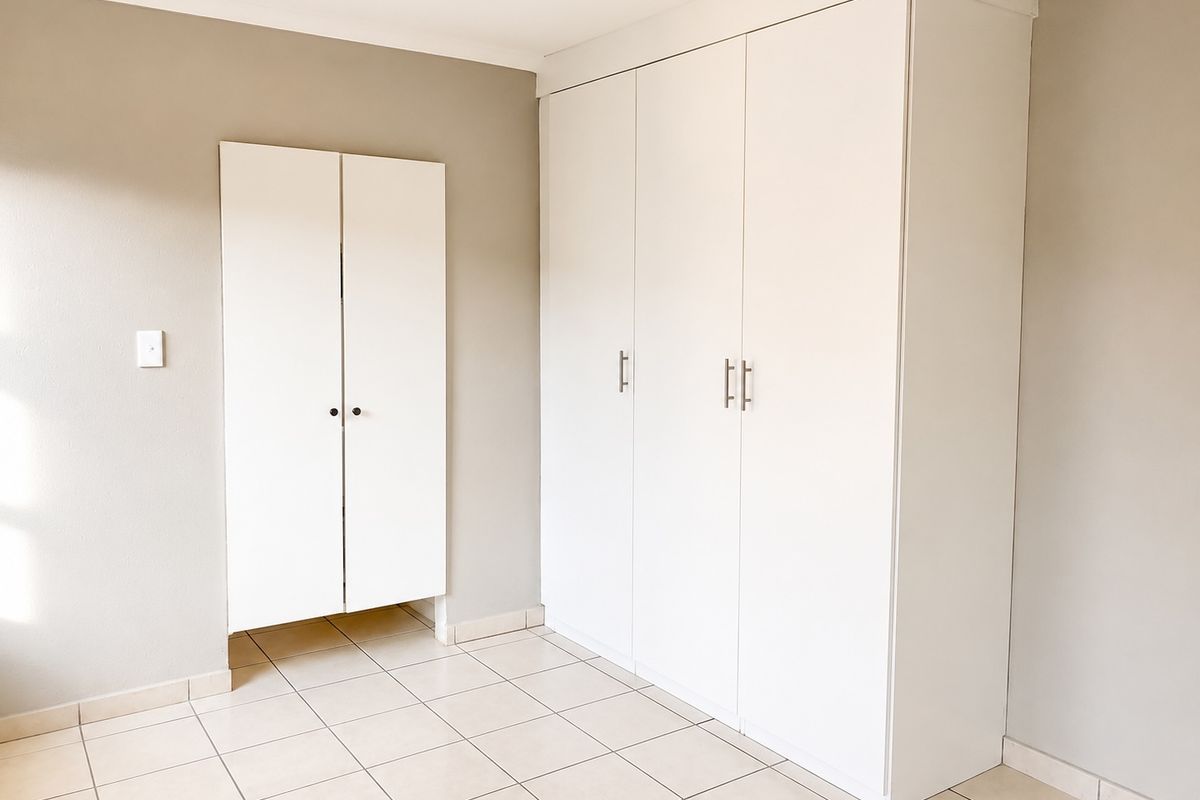 A clean, empty bedroom featuring neutral wall tones, tiled flooring, and ample built-in cupboard storage space.