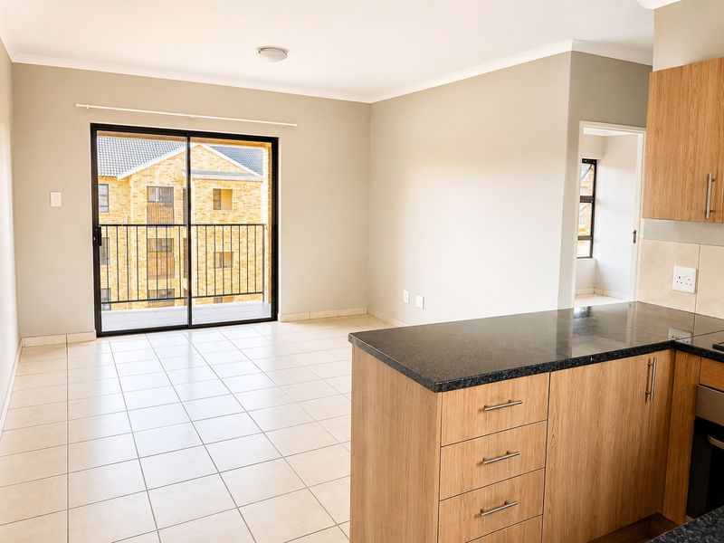 Open-plan living area featuring tiled floors, modern wood-finish kitchen cabinetry with granite countertops, and a sliding door leading to a private balcony.