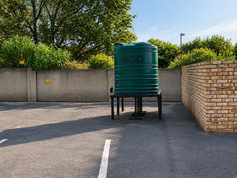 An outdoor utility area featuring a green water storage tank mounted on a metal stand, situated within a paved parking or service space.