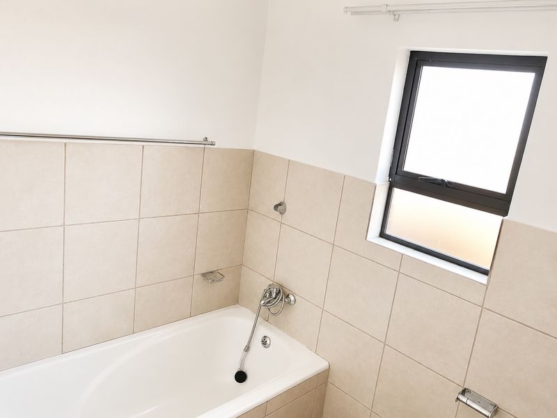A clean, modern bathroom featuring a built-in bathtub with tiled surround, handheld shower mixer, and a functional aluminium window.