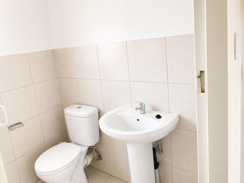 A clean and functional bathroom featuring a white pedestal washbasin, a standard toilet, and neutral ceramic wall tiling.