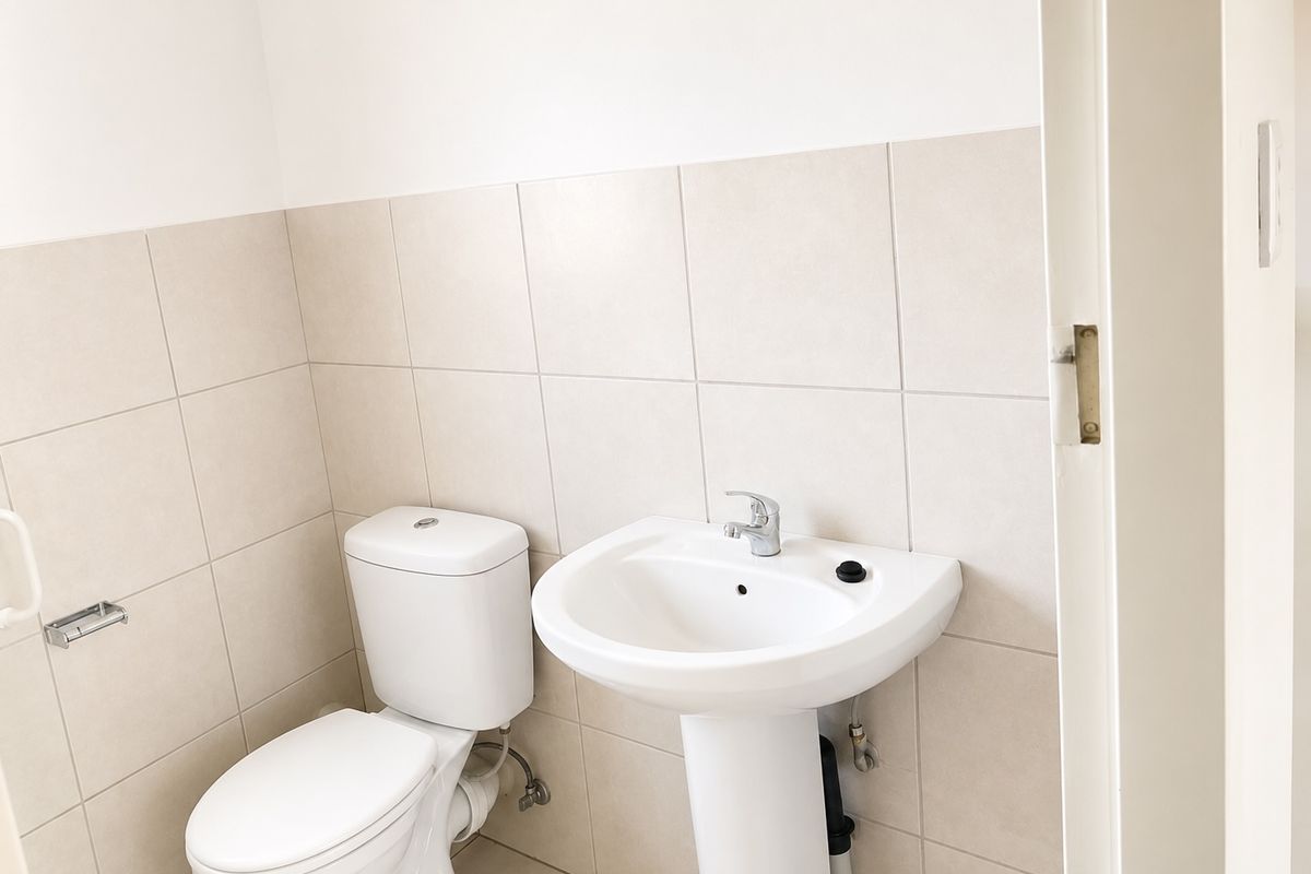 A clean and functional bathroom featuring a white pedestal washbasin, a standard toilet, and neutral ceramic wall tiling.