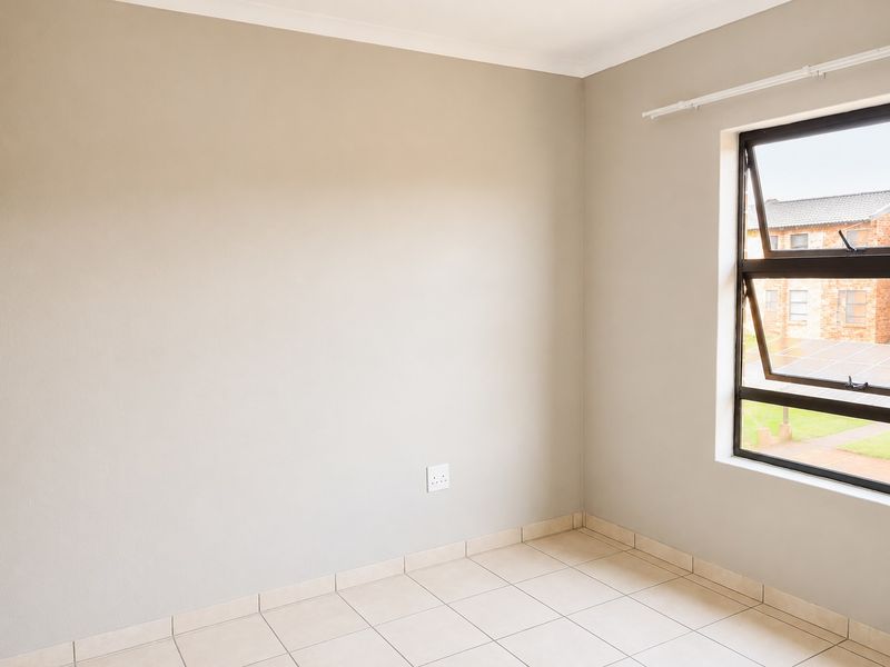 A clean, empty bedroom featuring neutral wall paint, tiled flooring, and a modern aluminium window frame.