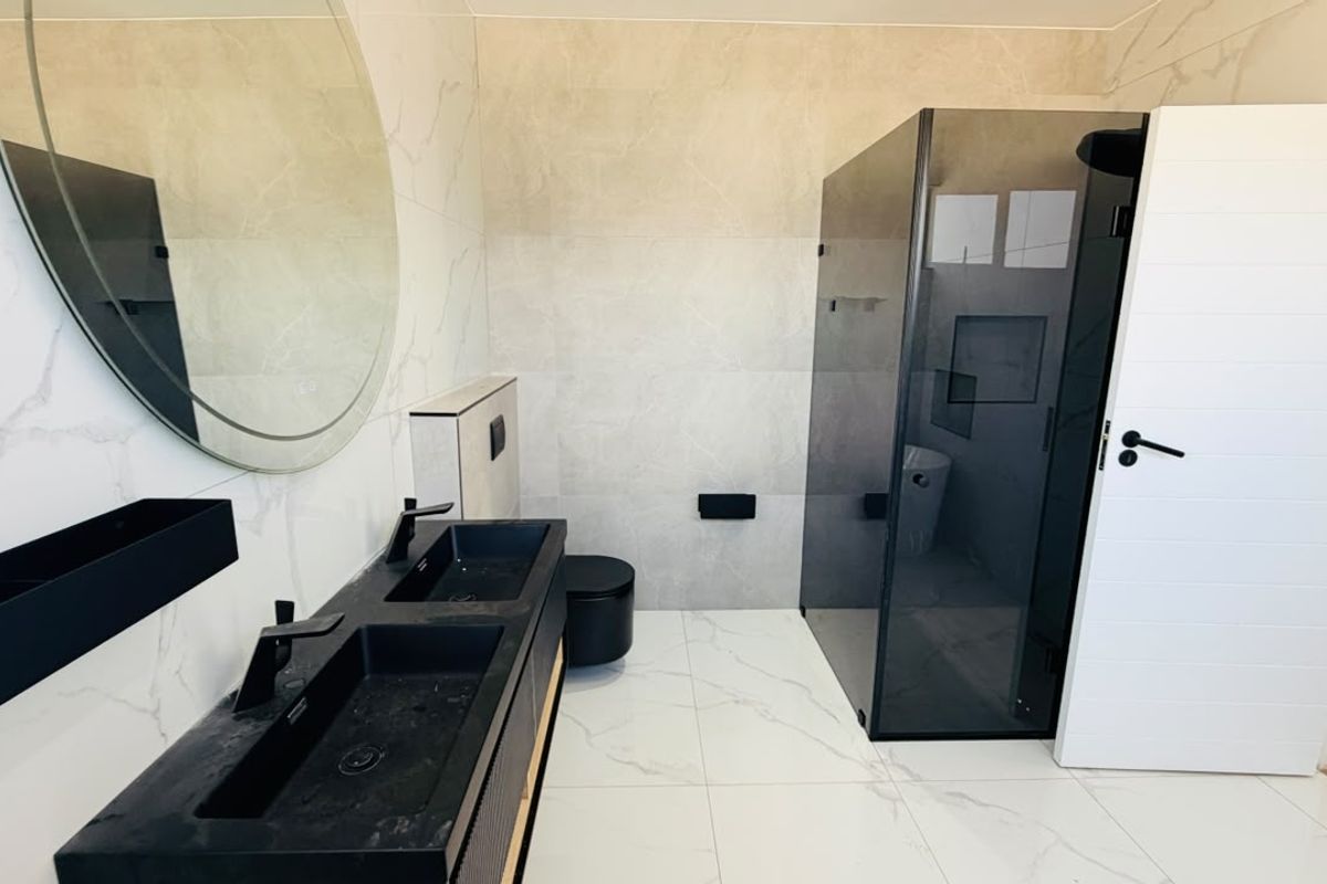 Modern bathroom featuring a double vanity with black basins, a walk-in glass shower, and large-format marble-look wall and floor tiles.