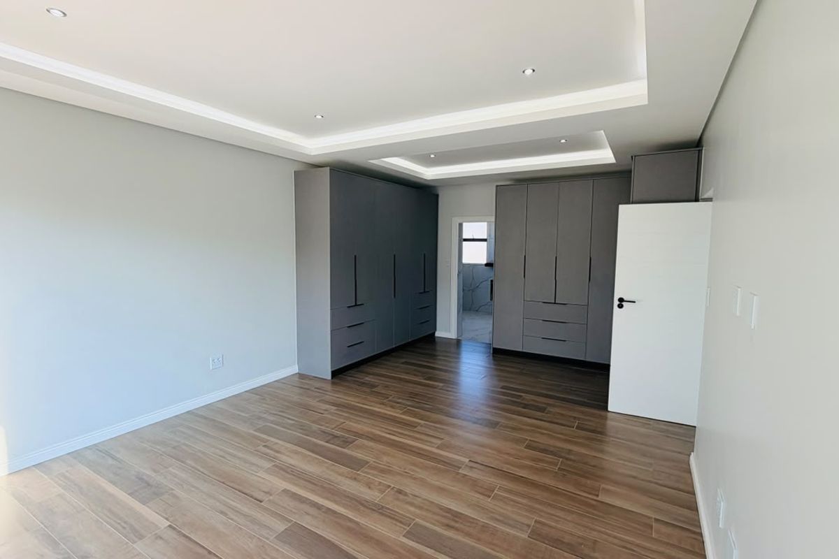 Spacious bedroom featuring modern wood-look tile flooring, recessed tray ceiling with integrated lighting, and extensive built-in grey cabinetry for ample storage.