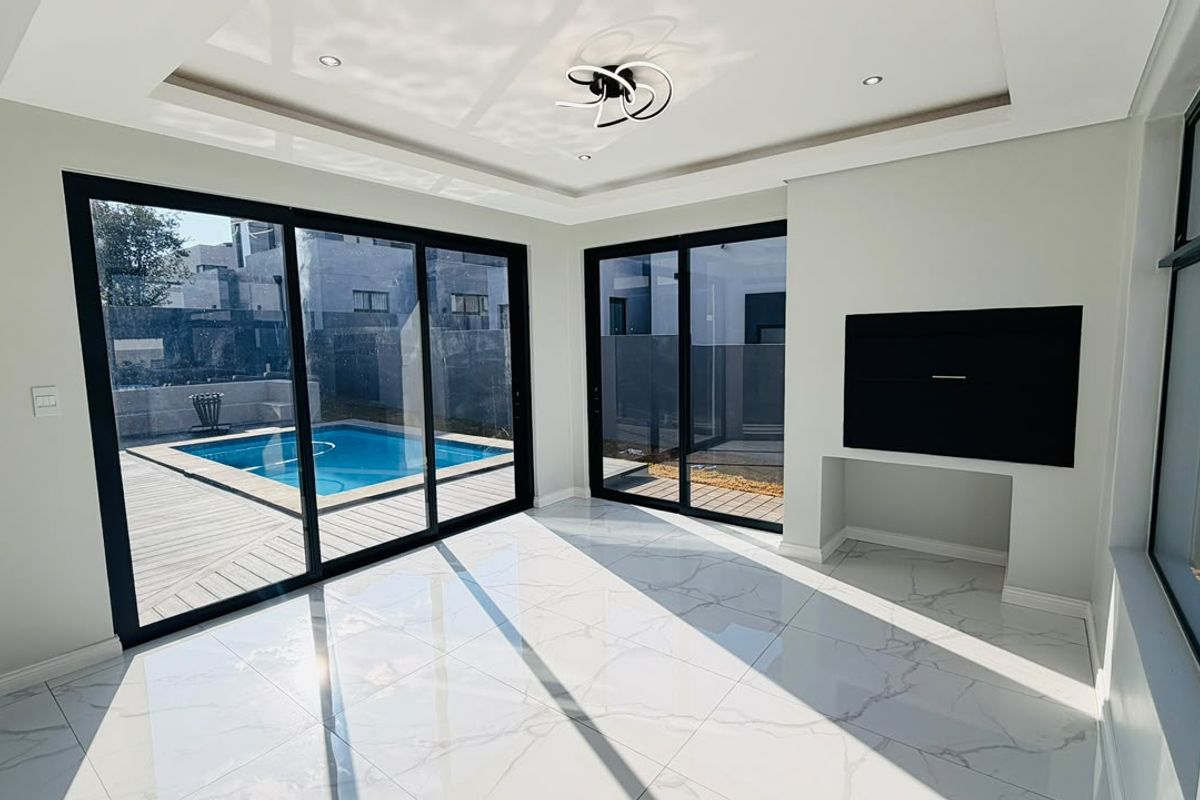 Modern living area featuring large sliding glass doors, polished marble-look floor tiles, recessed ceiling lighting, and a built-in media wall overlooking the pool area.