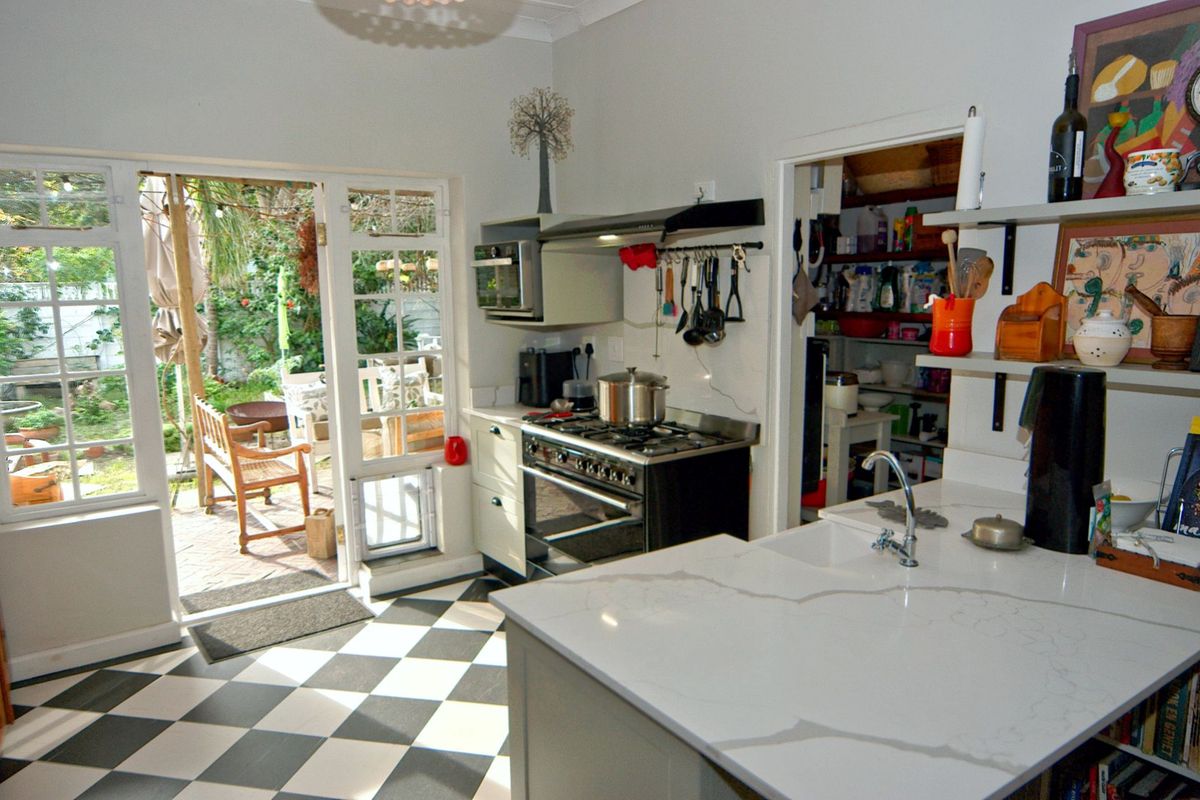 A functional kitchen featuring stone countertops, a gas stove, and direct access to the outdoor patio area, with an adjacent scullery.