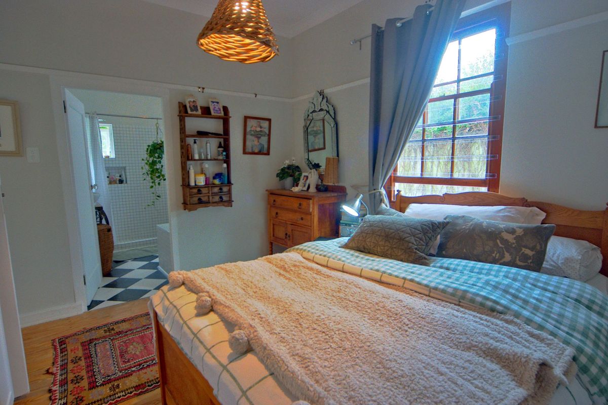 A cozy bedroom featuring timber flooring, picture rails, and direct access to an en-suite bathroom with classic checkered tiling.