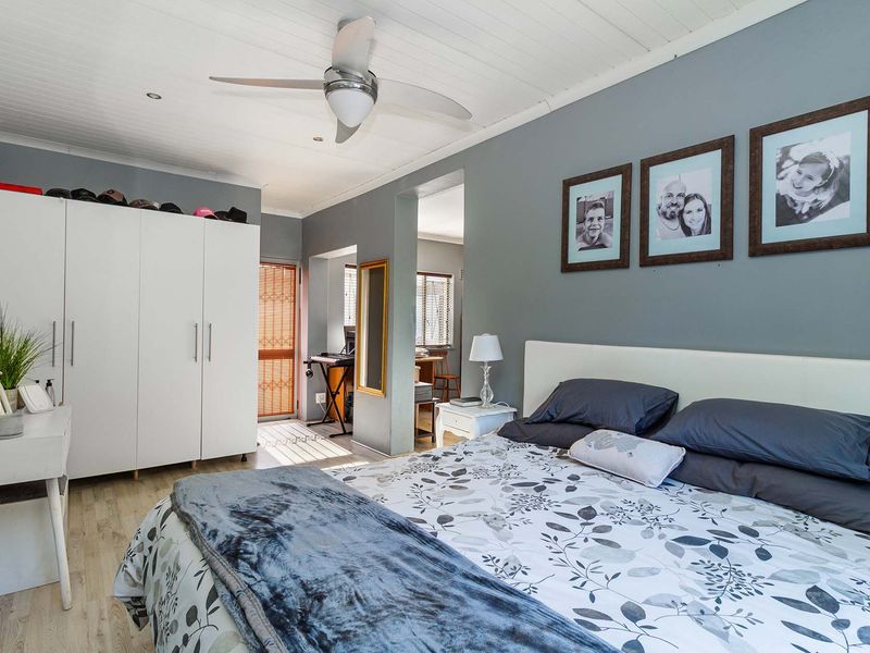 A well-maintained bedroom featuring laminate flooring, a ceiling fan, and a large built-in wardrobe with a neutral grey wall finish.