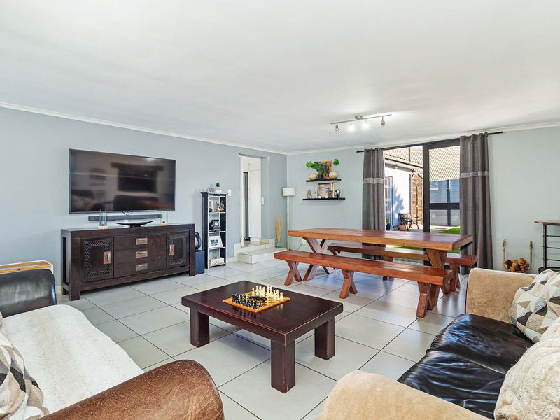 Spacious open-plan living and dining area featuring neutral tiled flooring, modern track lighting, and direct access to the outdoor patio through sliding glass doors.