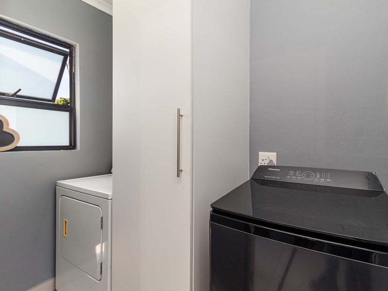 A functional laundry room featuring built-in cabinetry, space for a washing machine and tumble dryer, and a window for natural ventilation.