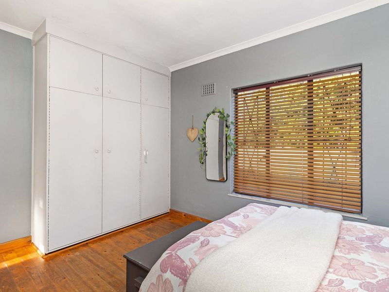 A bedroom featuring original timber flooring, built-in cupboards, and a window fitted with venetian blinds.