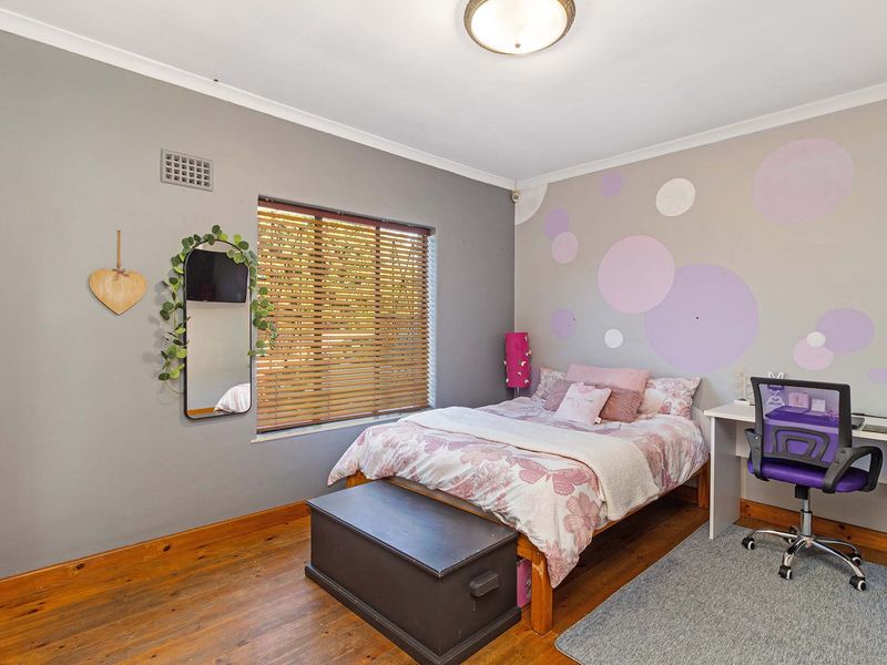 A bedroom featuring polished timber flooring, a window with venetian blinds, and a ceiling light fixture.