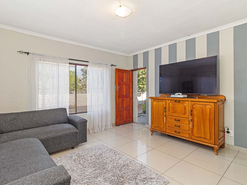 A living room featuring tiled flooring, a wooden entrance door, and a striped accent wall, providing a functional and well-lit living space.