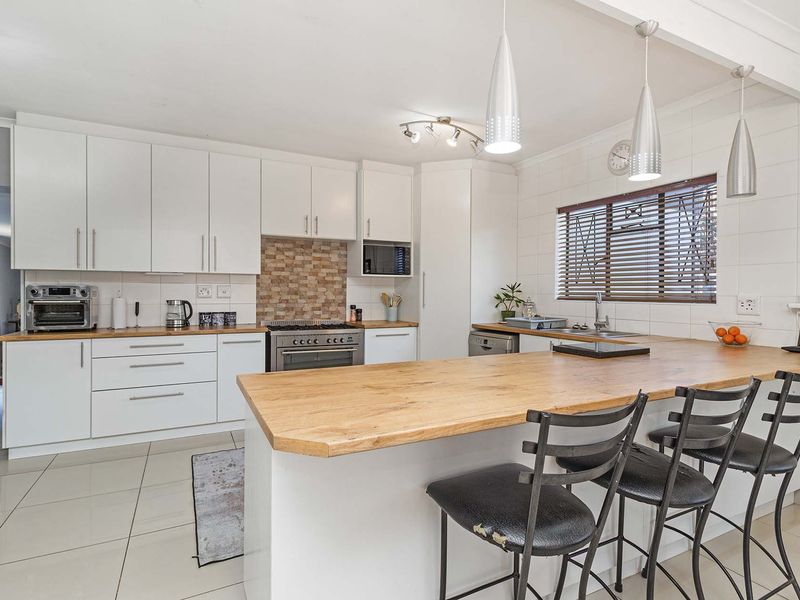 Modern kitchen featuring white cabinetry, wooden countertops, a breakfast bar, and integrated appliances, complemented by tiled flooring and contemporary pendant lighting.