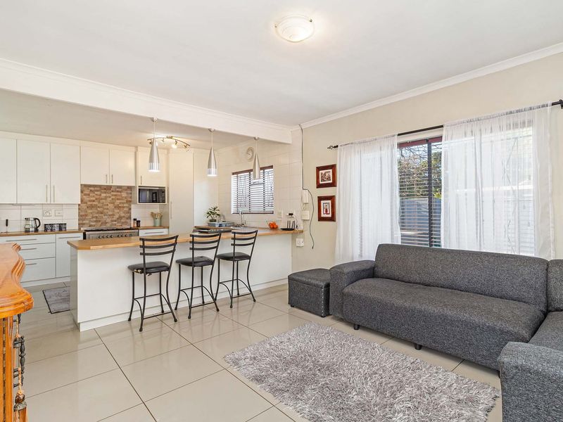 Open-plan living area featuring a modern kitchen with white cabinetry, breakfast bar, and tiled flooring, seamlessly flowing into the lounge space.