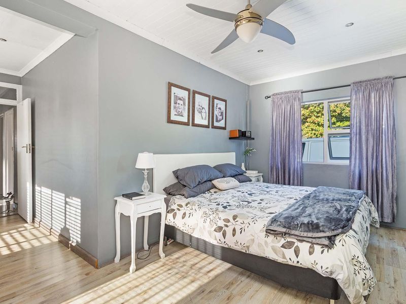 A well-maintained bedroom featuring light laminate flooring, a timber panelled ceiling with a central fan, and natural light through an aluminium-framed window.
