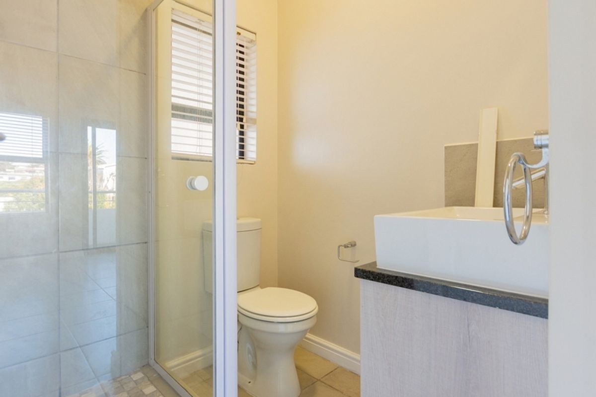 A clean and modern bathroom featuring a glass-enclosed shower, a vessel sink with a granite vanity top, and neutral tiled flooring.