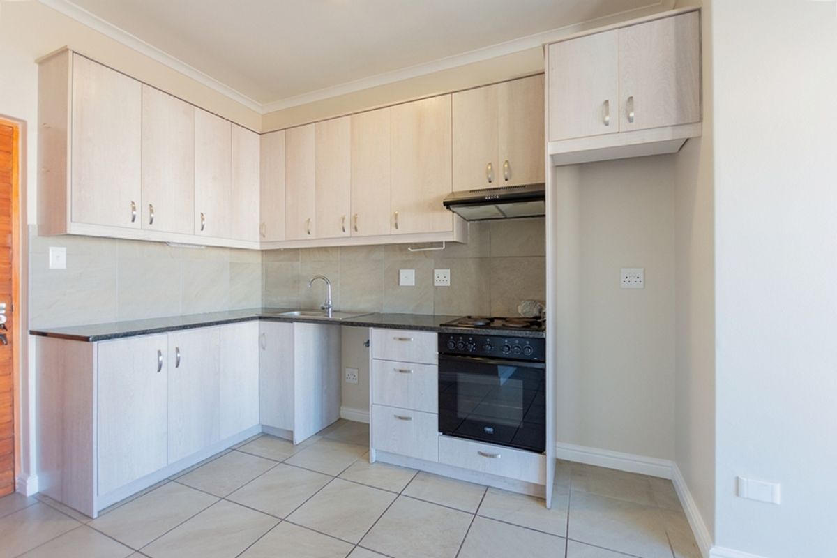 A clean, modern kitchen featuring light wood-finish cabinetry, stone countertops, tiled backsplash, and integrated oven with extractor fan.