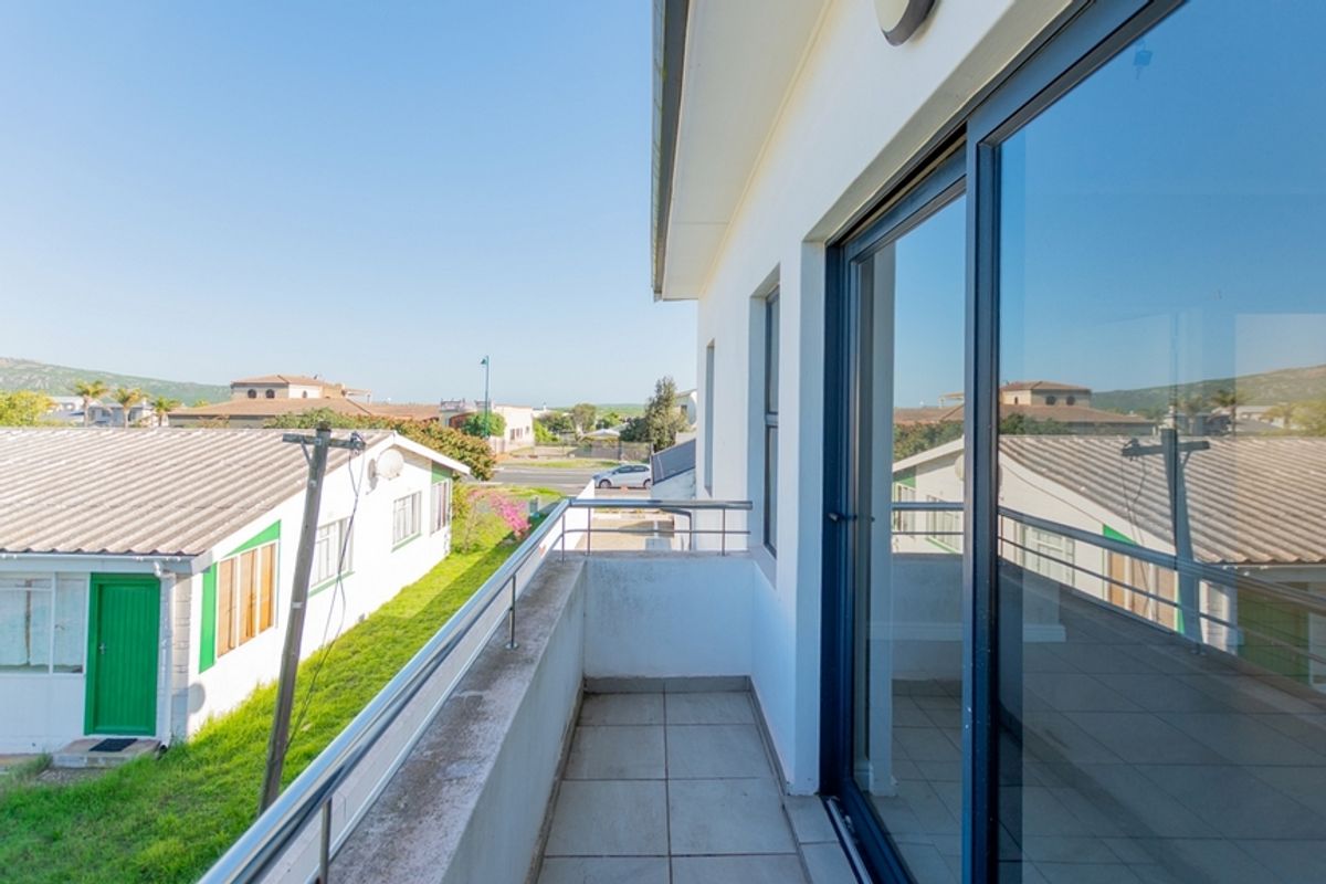 A balcony featuring tiled flooring and a stainless steel balustrade, accessible via large sliding glass doors, offering an elevated view of the surrounding area.