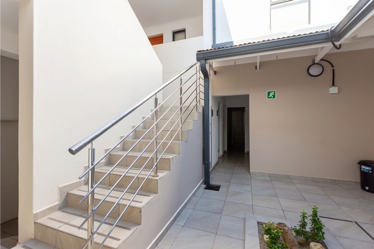 An exterior rear courtyard area featuring a tiled staircase with a stainless steel balustrade and paved flooring.