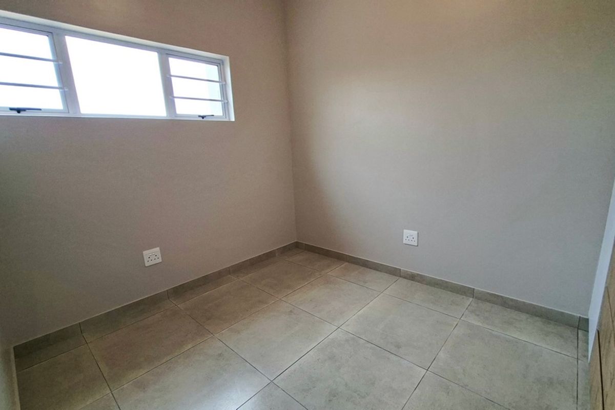 A clean, empty bedroom featuring neutral tiled flooring, a horizontal sliding window with security bars, and smooth painted walls.