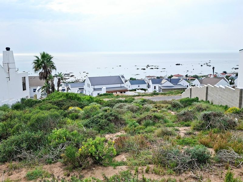 A view of a vacant residential plot overlooking a coastal neighborhood and the ocean.