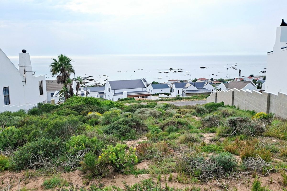 A view of a vacant residential plot overlooking a coastal neighborhood and the ocean.