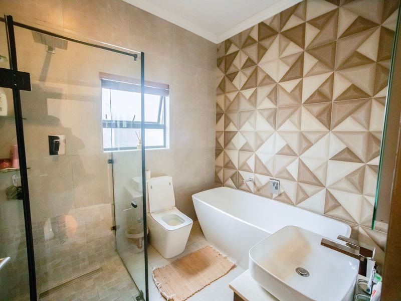 Modern bathroom featuring a freestanding bathtub, glass-enclosed shower, wall-mounted toilet, and a stylish geometric tiled feature wall.