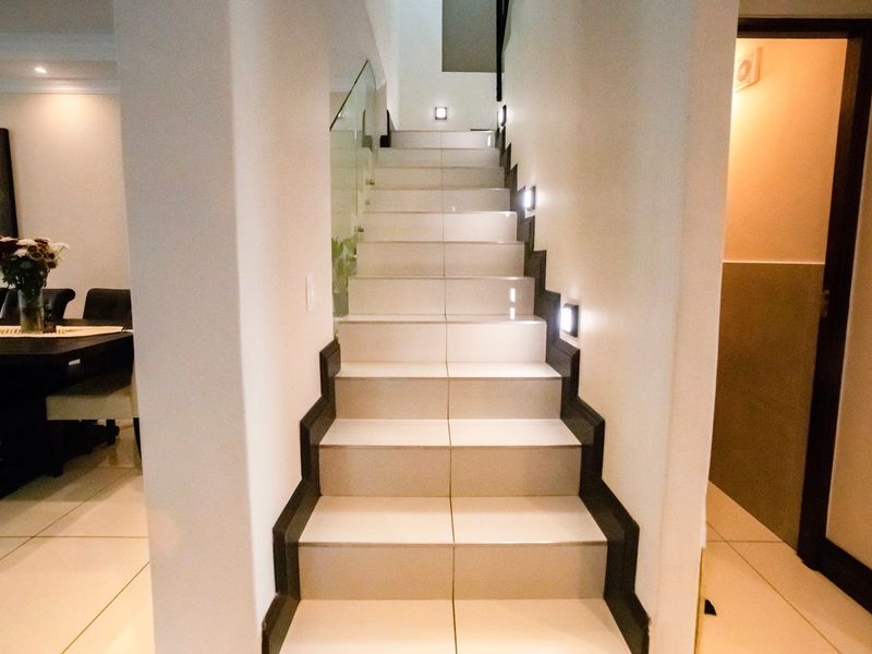 A modern staircase featuring tiled steps, a sleek glass balustrade, and integrated recessed lighting, providing a clean and contemporary transition between levels.