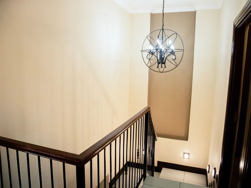 A well-lit staircase featuring a decorative wrought iron balustrade, wooden handrail, and a modern spherical pendant light fixture.