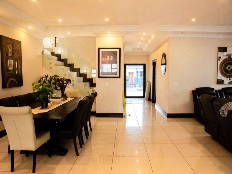 Spacious open-plan living and dining area featuring polished porcelain floor tiles, recessed downlighting, and a modern staircase with a glass balustrade.