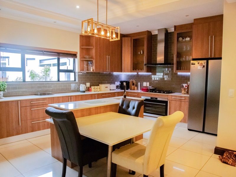 Modern kitchen featuring wood-finish cabinetry, stone countertops, a central island, and integrated appliances, complemented by stylish pendant lighting and a tiled backsplash.