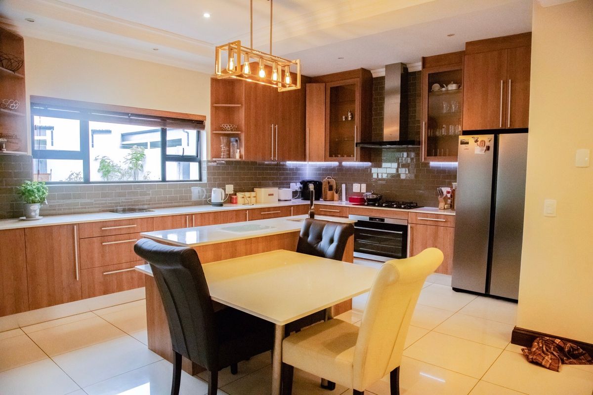 Modern kitchen featuring wood-finish cabinetry, stone countertops, a central island, and integrated appliances, complemented by stylish pendant lighting and a tiled backsplash.
