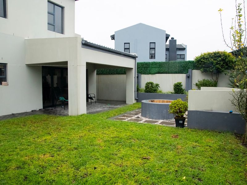 A well-maintained rear garden featuring a covered patio area, a built-in circular fire pit, and a neat lawn with perimeter boundary walls.