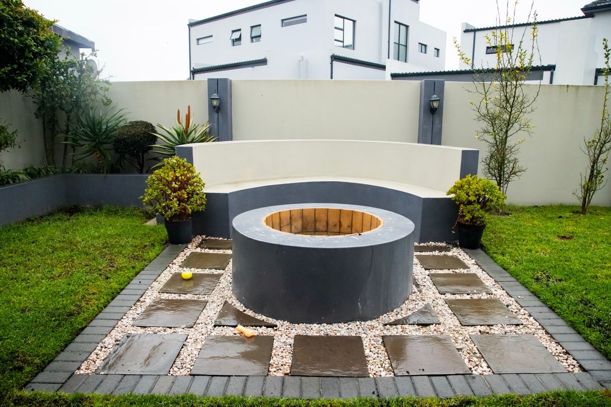 A well-maintained rear garden area featuring a circular built-in fire pit with a curved concrete bench and stone paved surround.